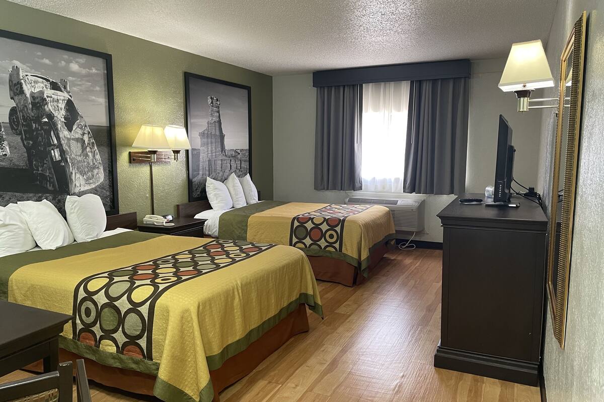 A hotel room with two beds, a desk, a TV, and a window with curtains.