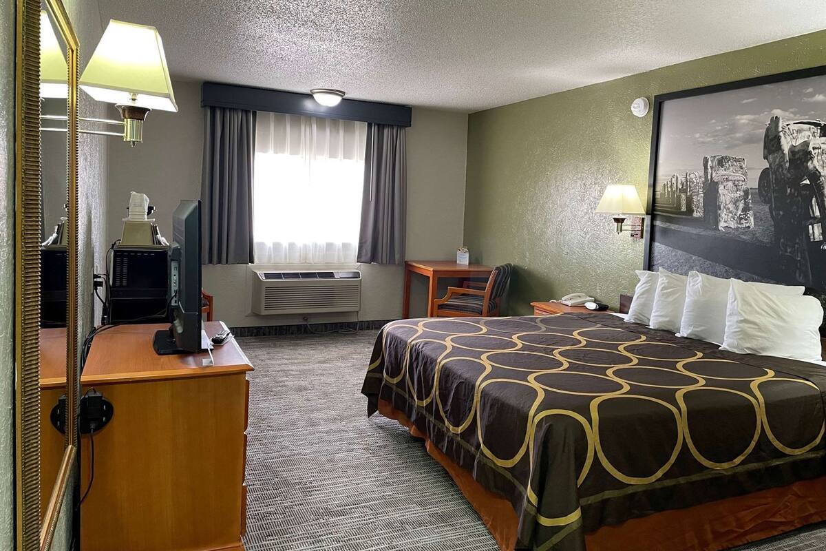 A hotel room with a bed, desk, chair, air conditioning unit, and a large framed picture on the wall.