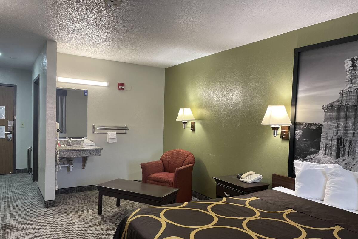 A hotel room with a bed, a desk, a chair, a bathroom, and a painting on the wall.