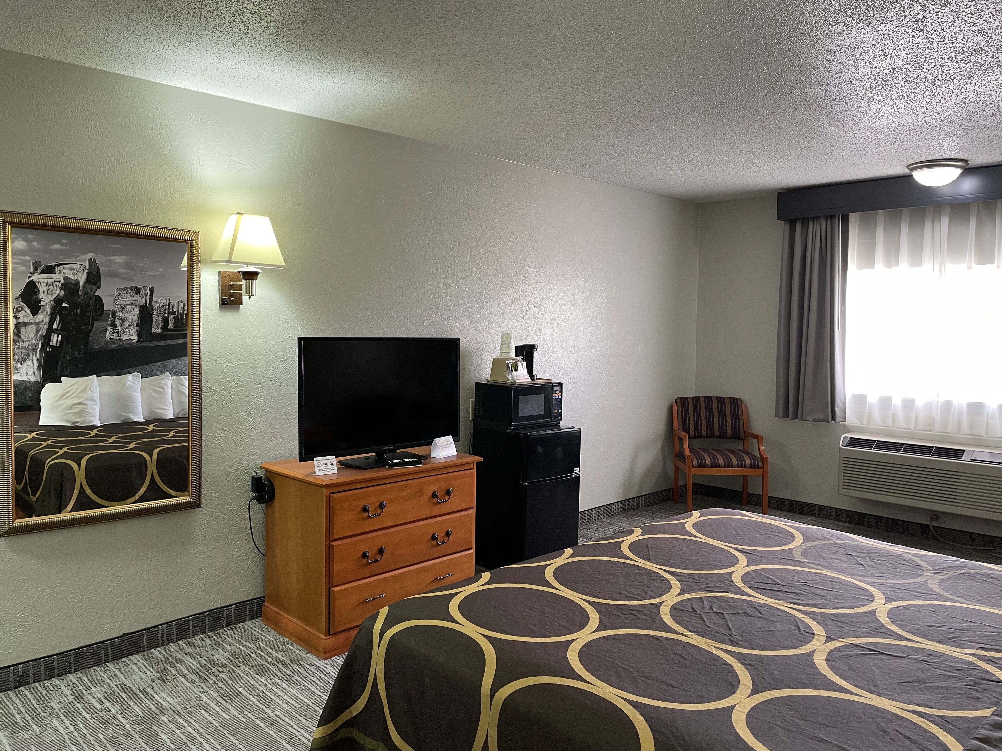 Ein Hotelzimmer mit Bett, Fernseher, Schminktisch, Stuhl und einem Fenster mit Vorhängen.