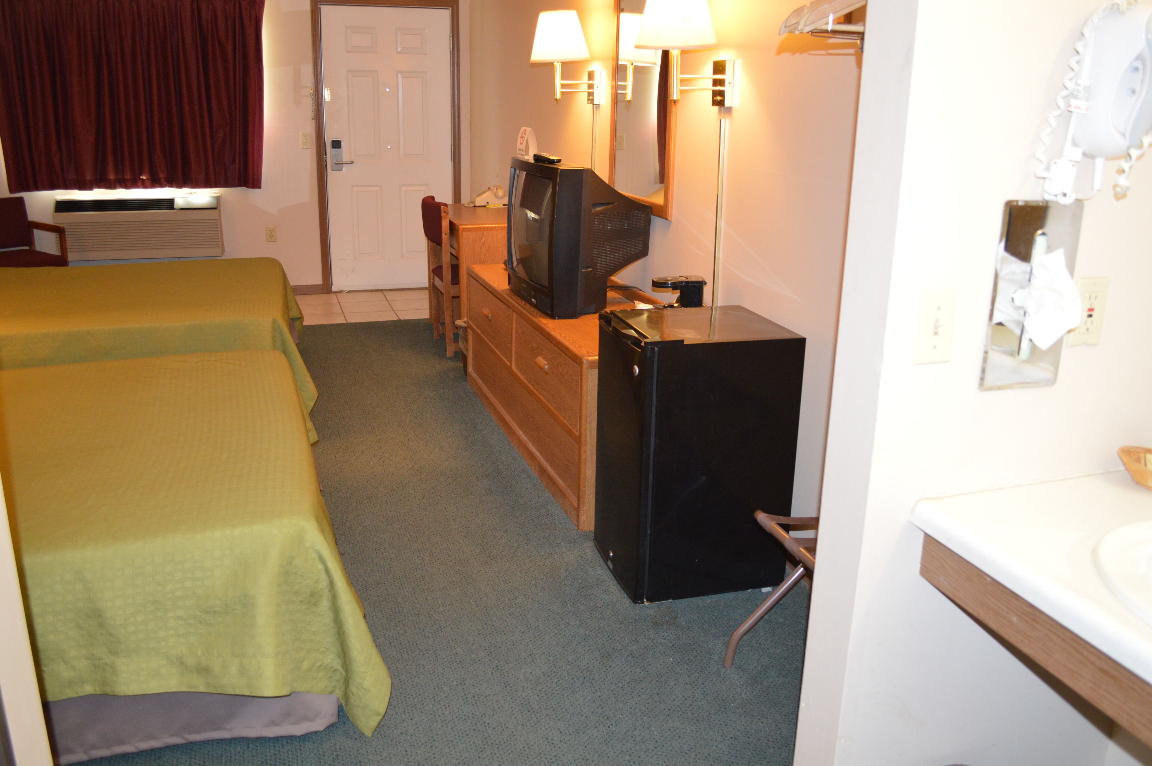 A hotel room with two beds, a small desk with a television, a mirror, a hairdryer, and a sink.