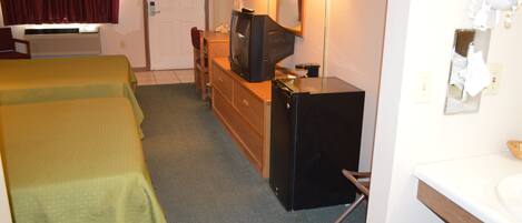 A hotel room with two beds, a small desk with a television, a mirror, a hairdryer, and a sink.