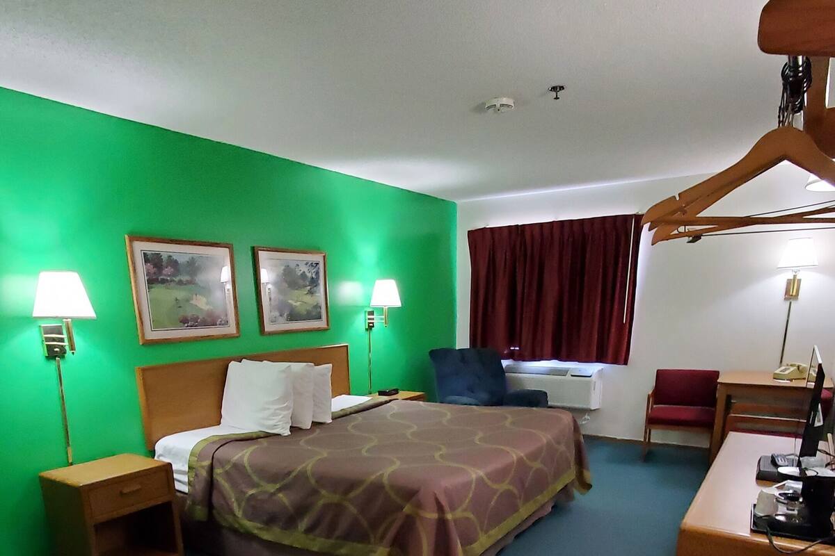 Habitación de hotel con cama, dos lámparas de noche, un escritorio con computadora, una silla y un ventanal con cortinas.