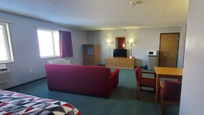 Habitación de hotel con cama, sofá rojo, mesa de madera, televisor, microondas y una pequeña kitchenette.