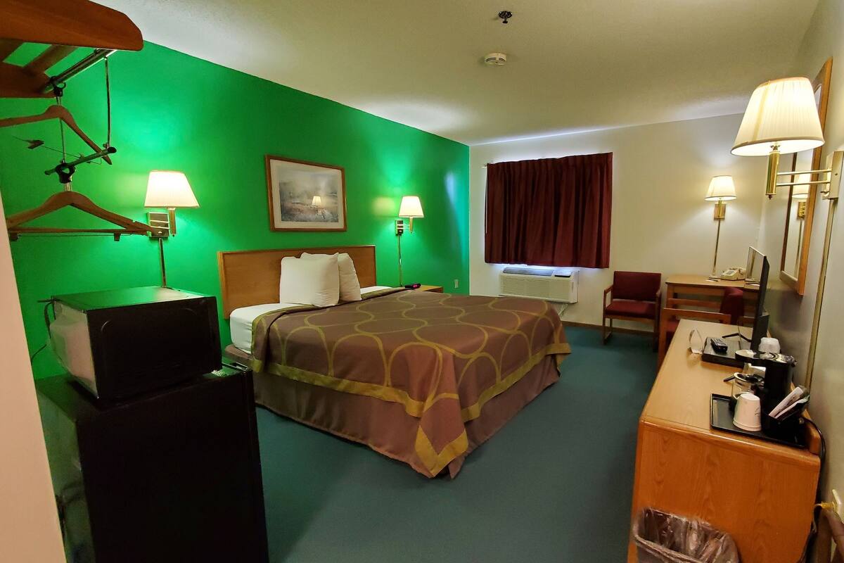 Una habitación de hotel con una cama, un escritorio con computadora, una silla, un cesto de basura y un espejo.