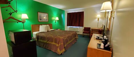 Une chambre d’hôtel comprenant un lit, un bureau avec un ordinateur, une chaise, une poubelle et un miroir.
