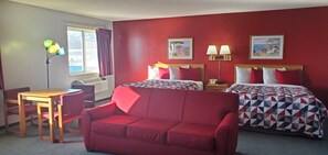 Quarto de hotel com duas camas, um sofá vermelho, uma mesa de madeira e uma escrivaninha.
