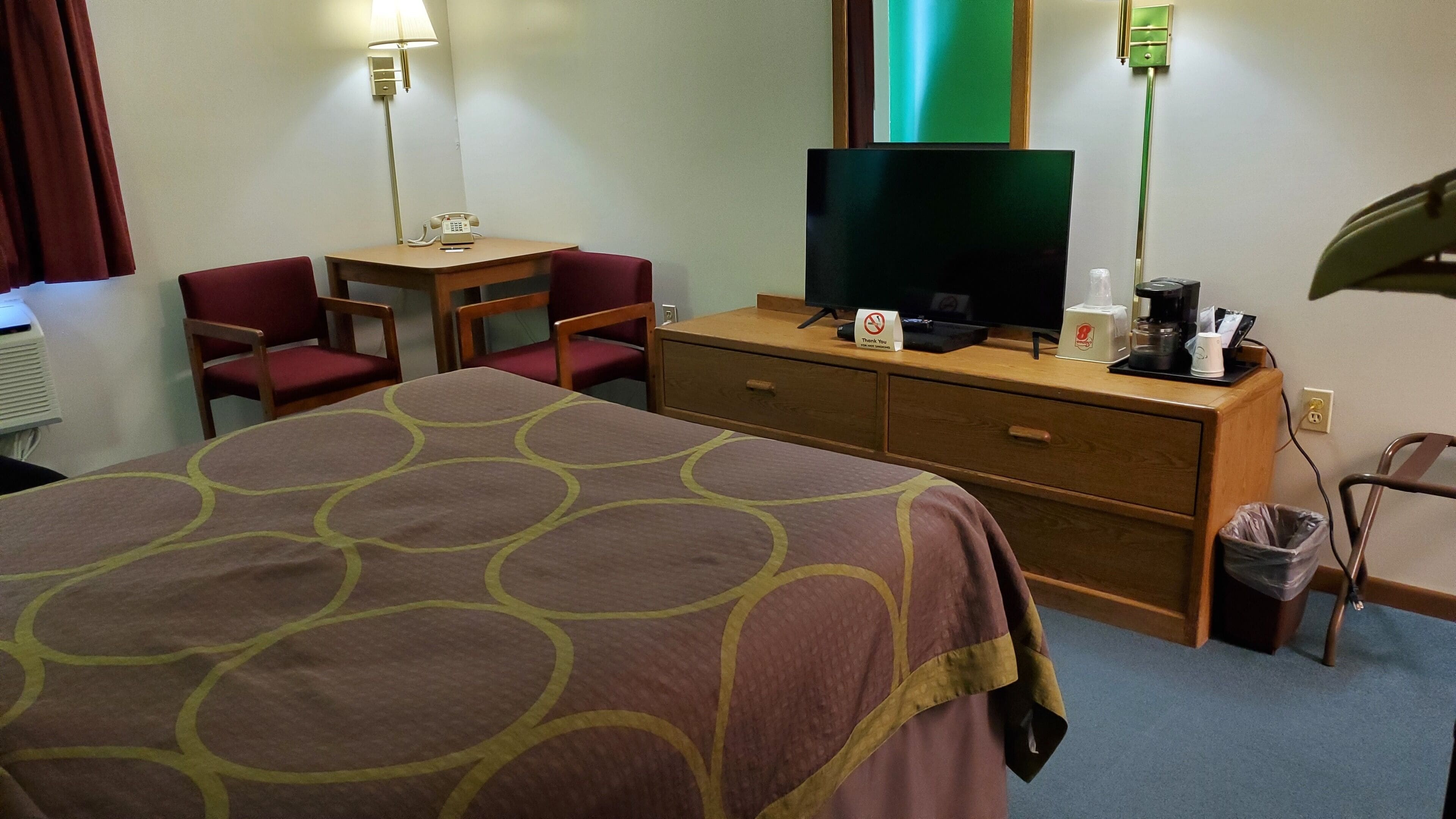A hotel room with a bed, a desk with a telephone, a television, and a trash bin.