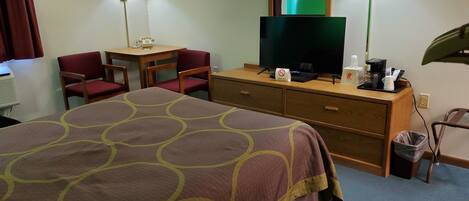 A hotel room with a bed, a desk with a telephone, a television, and a trash bin.