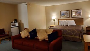 Una habitación de hotel con un sofá rojo, una cama con colcha estampada, un escritorio pequeño, un microondas y dos cuadros en la pared.