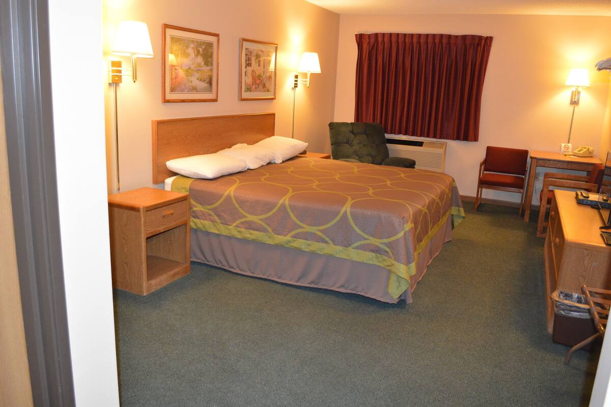 Una habitación de hotel con cama, escritorio, silla, mesita de noche y dos lámparas de pared.