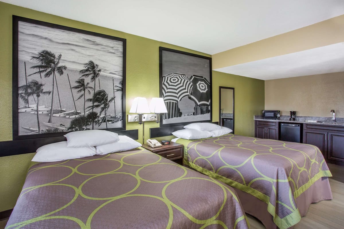 Une chambre d’hôtel avec deux lits, un bureau, une chaise, une lampe et des œuvres d’art accrochées aux murs.