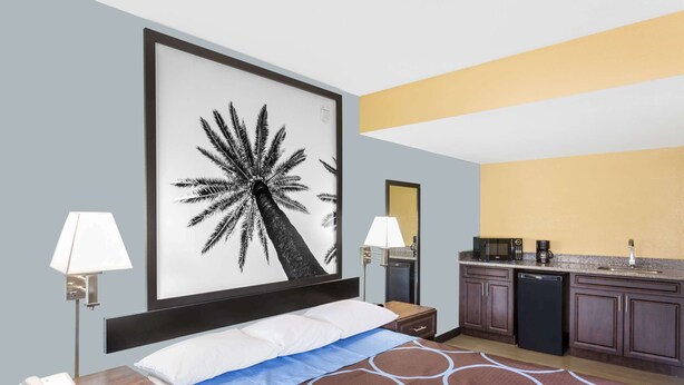 Een hotelkamer met een bed, nachtlampjes, een groot gepresenteerd schilderij, een kitchenette en een nachtkastje met een telefoon.