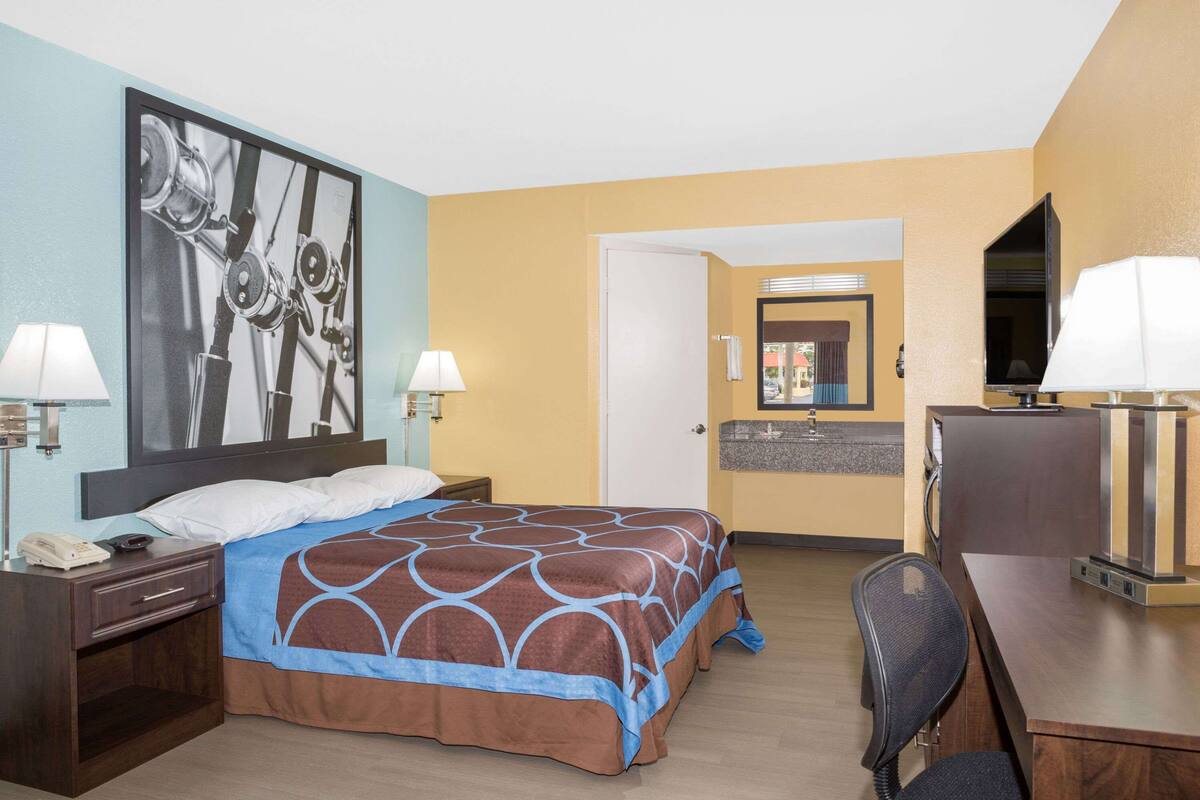 Une chambre d’hôtel avec un lit, un bureau, une chaise et une salle de bain visible à travers une porte ouverte.