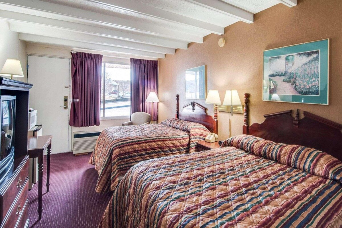 Een hotelkamer met twee bedden, een bureau met lamp, een stoel en een schilderij aan de muur.