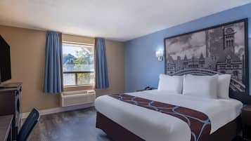 Ein Hotelzimmer mit einem großen Bett, einem Schreibtisch mit Computer, einem Fenster mit Vorhängen und einem Wandbild.