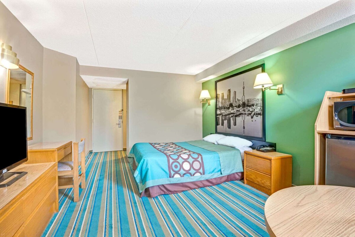 A hotel room with a bed, a desk with a TV, a chair, a microwave, and a door leading to another room.