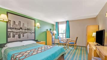 A hotel room with a bed, a desk, a chair, a television, and a window with curtains.