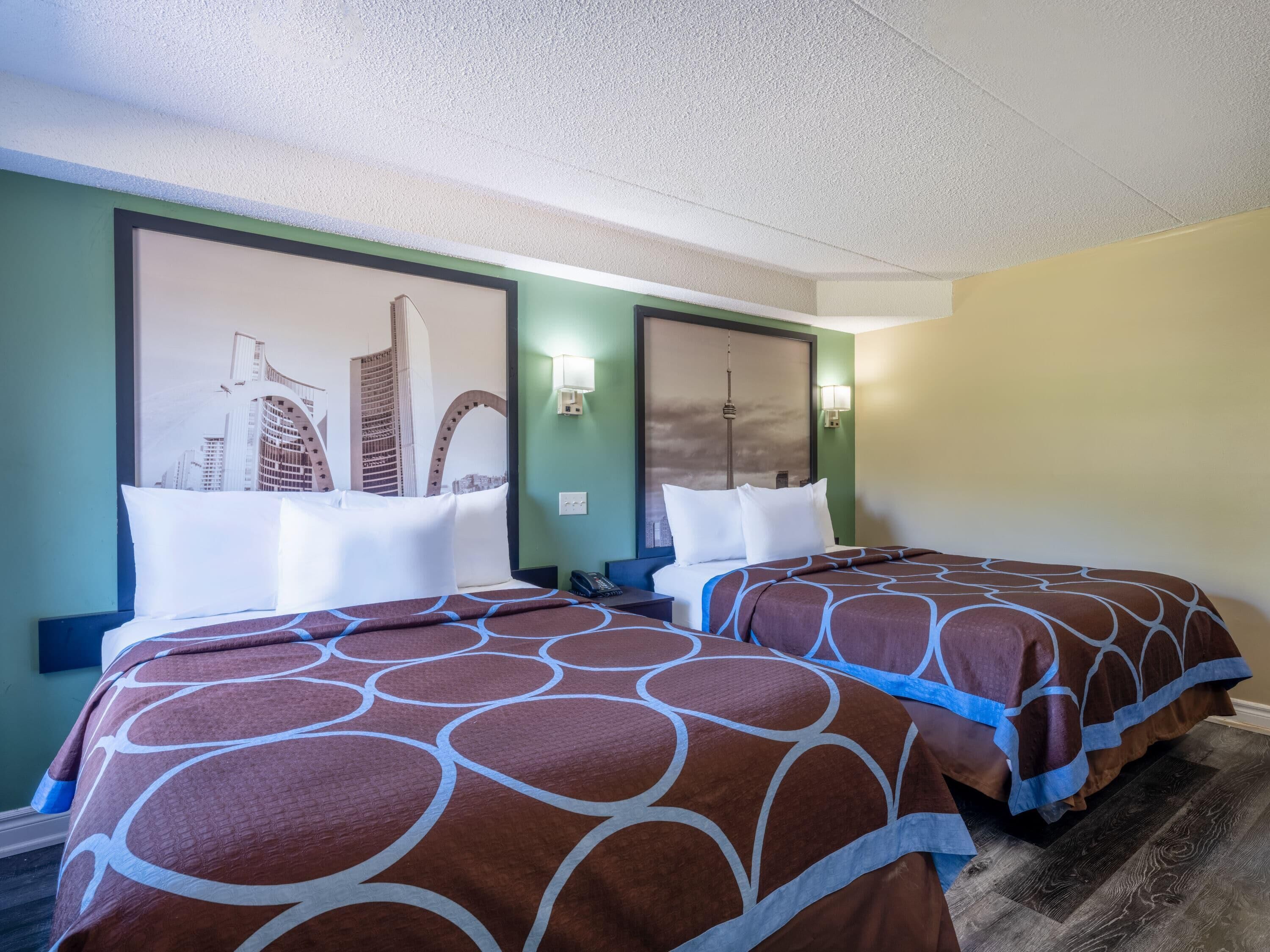 A hotel room with two beds, each with a brown and white patterned bedspread, a cityscape mural on the wall, and a phone on the nightstand.