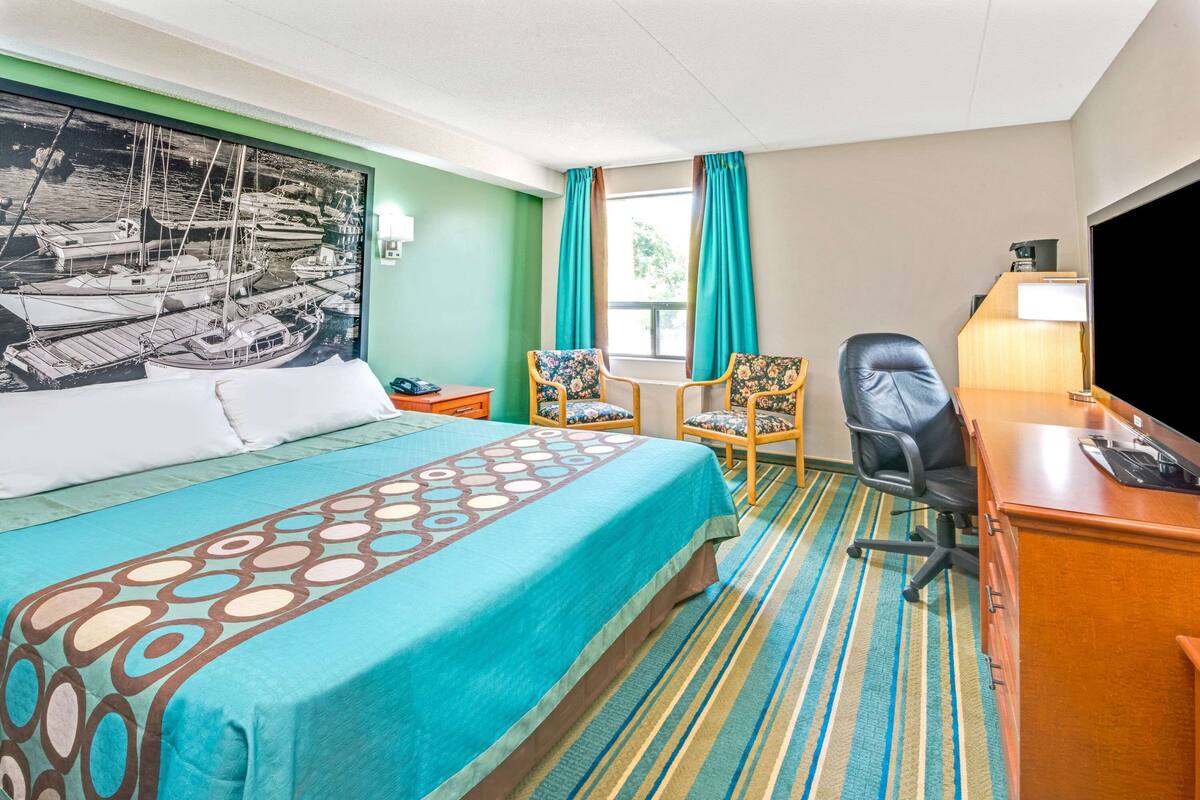 Ein Hotelzimmer mit Bett, Schreibtisch, Stuhl, Fernseher und einem Vorhangfenster.