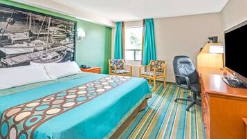 Una habitación de hotel con cama, escritorio, silla, televisión y ventana con cortinas.