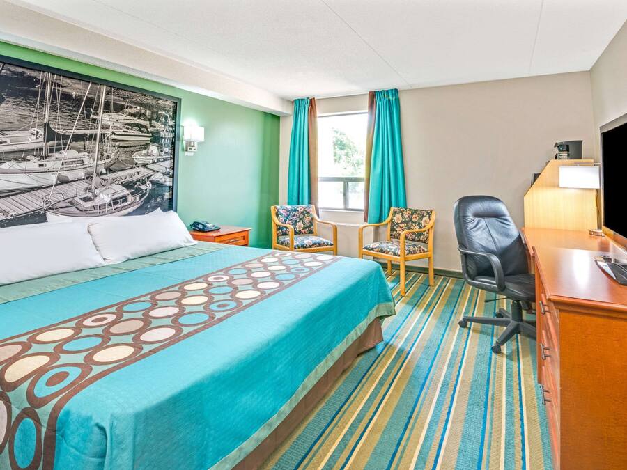 Una habitación de hotel con cama, escritorio, silla, televisión y ventana con cortinas.
