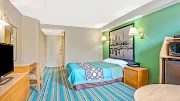 Una habitación de hotel con cama, escritorio con televisor, cómoda y lámpara de pared.