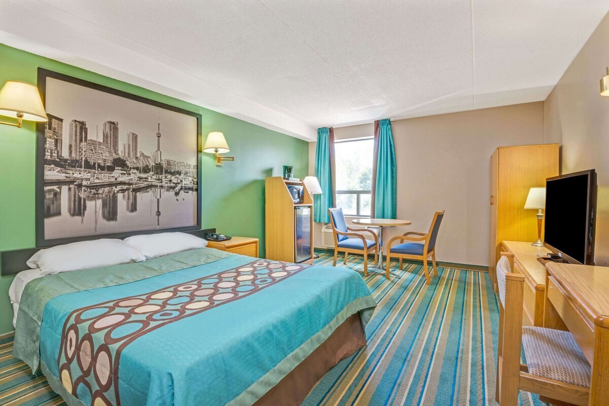 A hotel room with a bed, a desk, a chair, a television, and a window with curtains.
