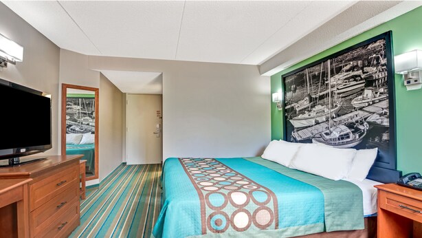 Een hotelkamer met een bed, een televisie, een dressoir en een schilderij van boten aan de muur.