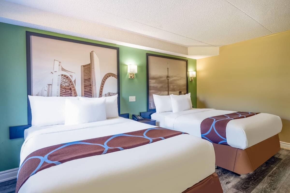 Ein Hotelzimmer mit zwei Betten, jeweils mit einem gemusterten Überwurf, einem Stadtbild-Wandgemälde und einem Nachttisch mit einem Telefon.