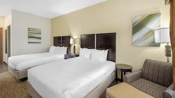 Ein Hotelzimmer mit zwei Betten, einem Sessel, einem kleinen Tisch und einer Lampe.