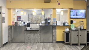 A reception area with a counter, a television screen displaying a video, and a sign indicating the use of personal protective equipment. - Best Western Plus The Four Corners Inn (Farmington)