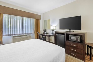 Habitación de hotel con cama, escritorio, televisión, microondas y ventana con cortinas.