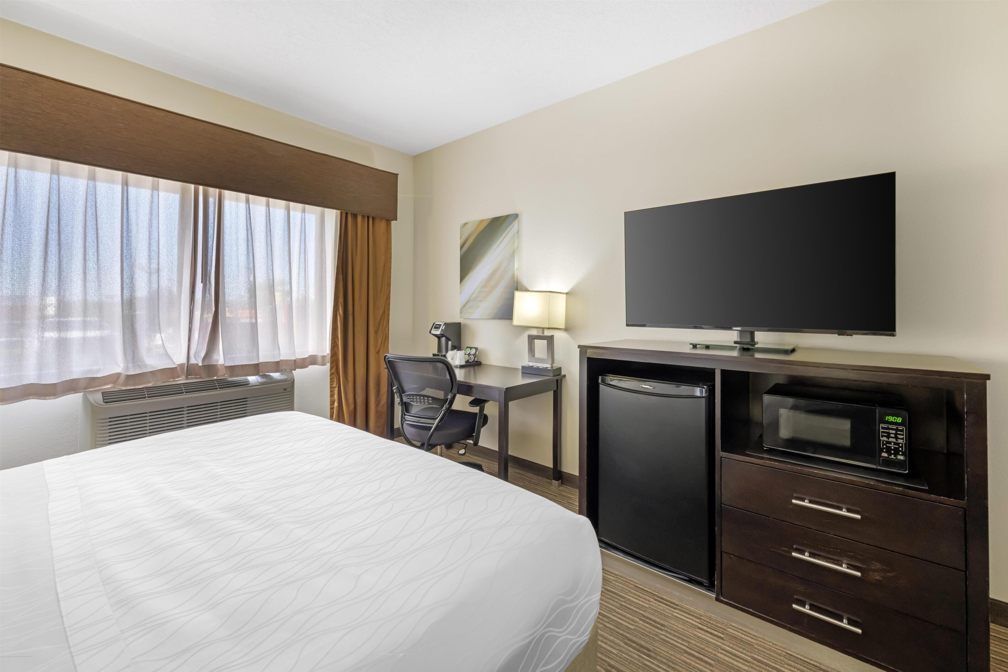 A hotel room with a bed, a desk with a chair, a television, a microwave, and a refrigerator.