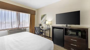 A hotel room with a bed, a desk with a chair, a television, a microwave, and a refrigerator.