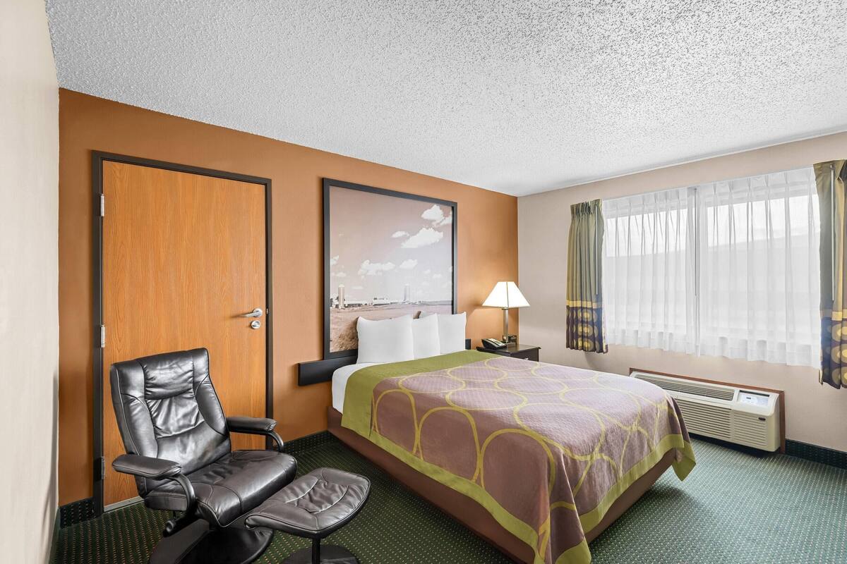 Habitación de hotel con cama, escritorio, silla, ventana con cortinas y aire acondicionado instalado en la pared.