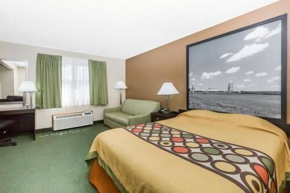 A hotel room with a bed, a desk, a chair, a lamp, and a large window with a view of a bridge.