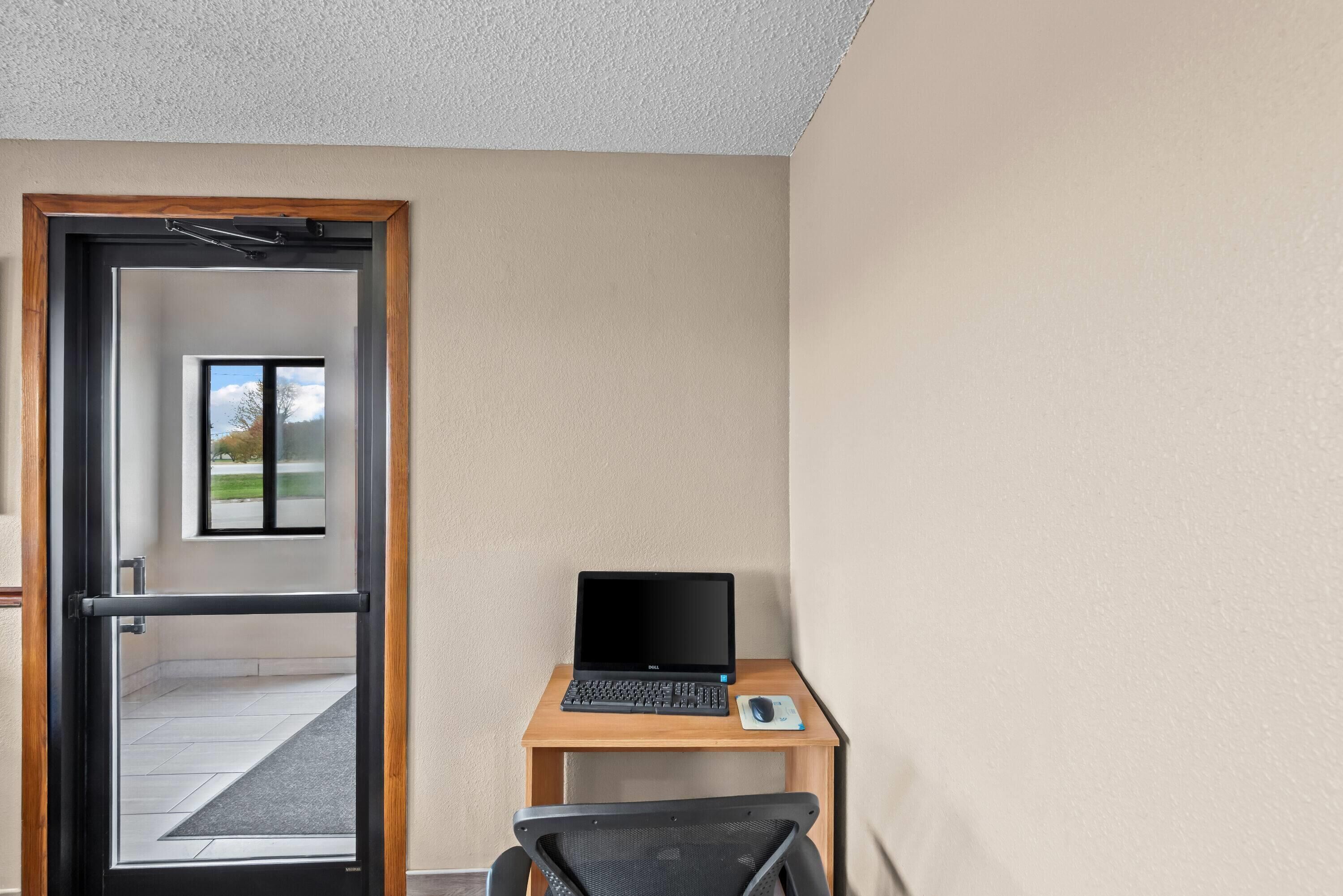 A room with a laptop on a wooden desk, a chair, and a door leading outside.