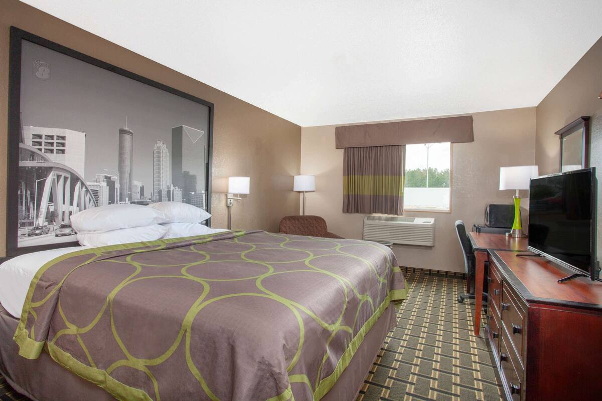 A hotel room with a large bed, a desk with a television, and a cityscape poster on the wall.