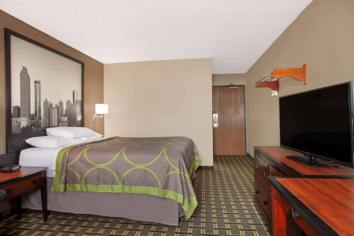 A hotel room with a bed, a television, a desk, and a wall-mounted TV.