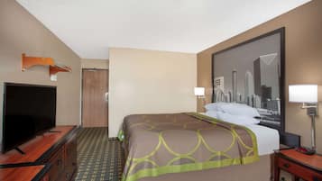 Quarto de hotel com uma cama, uma televisão sobre uma cômoda de madeira, um cartaz com vista para a cidade na parede e uma porta.