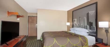 A hotel room with a bed, a television on a wooden dresser, a cityscape poster on the wall, and a door.