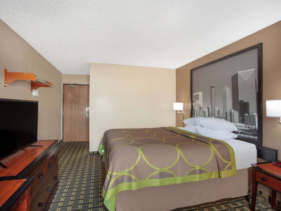 Quarto de hotel com uma cama, uma televisão sobre uma cômoda de madeira, um cartaz com vista para a cidade na parede e uma porta.
