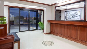 A reception area with a wooden reception desk, a large mirror, and a glass door leading outside. - Super 8 by Wyndham Waycross GA (Waycross)