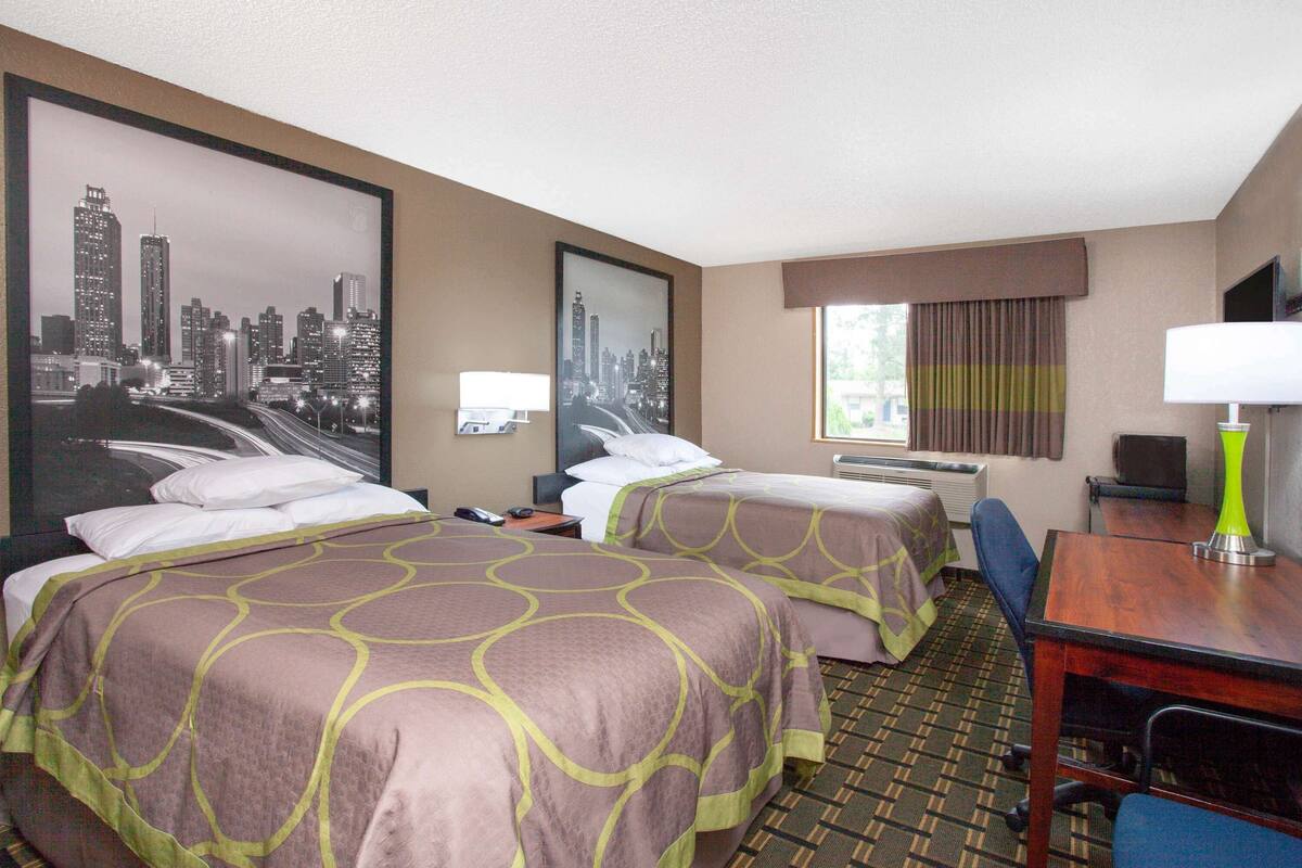 A hotel room with two beds, a desk, a chair, a television, and a window with curtains.
