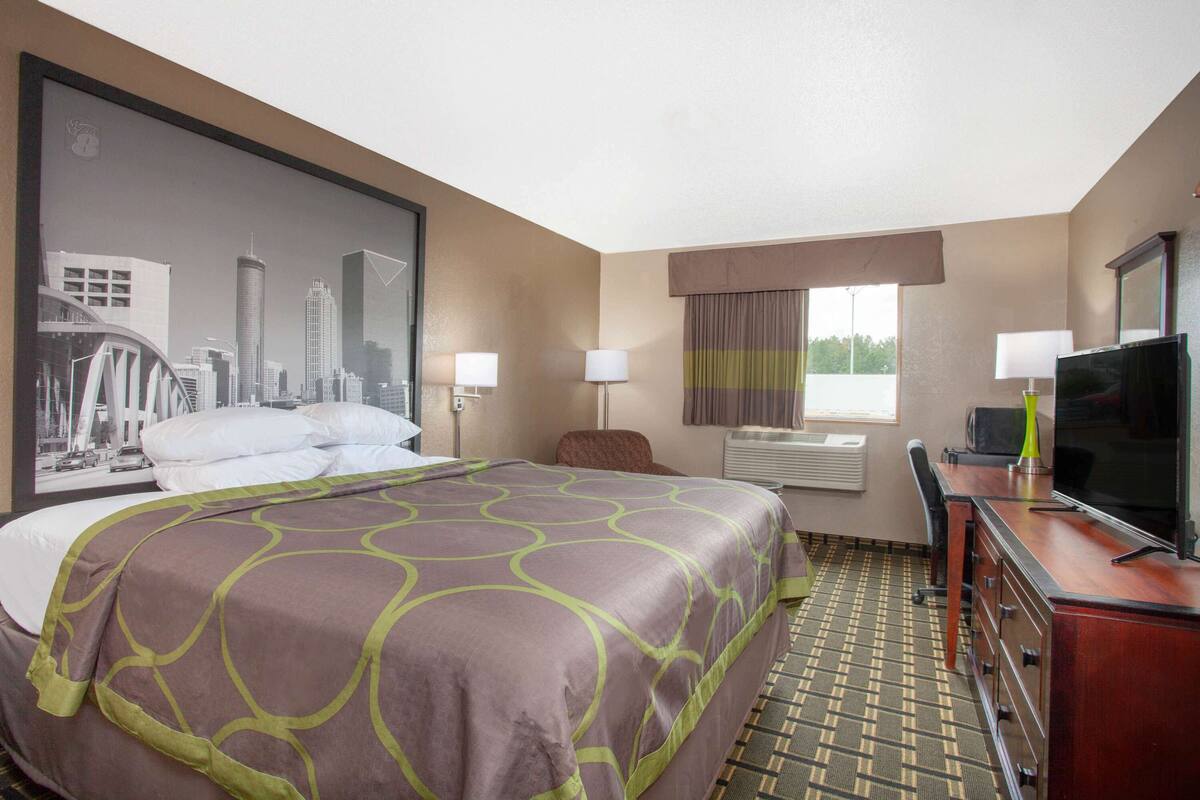 A hotel room with a large bed, a desk with a television, and a cityscape painting on the wall.
