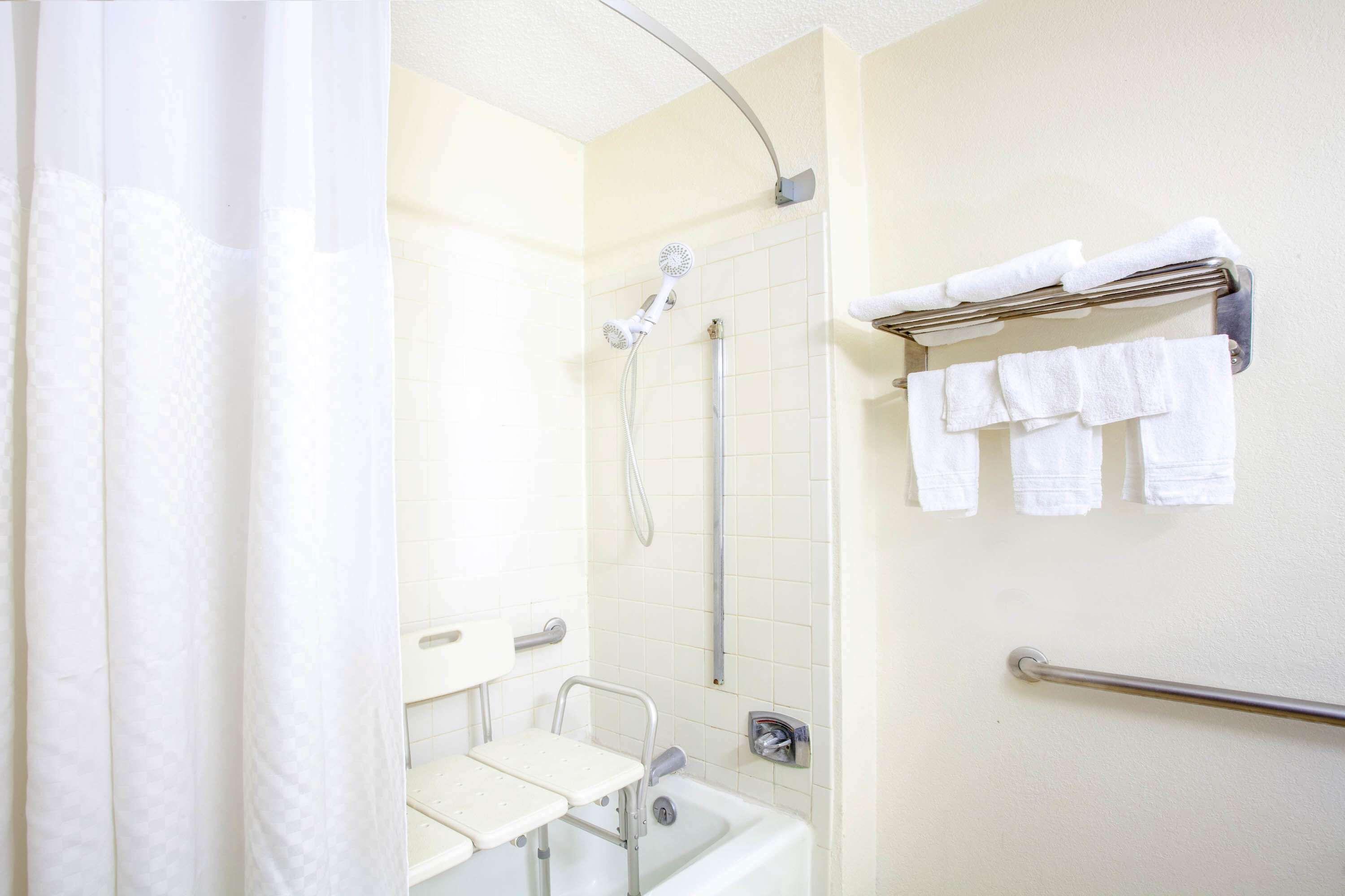 Un baño con ducha, barra de apoyo, toallero con toallas y un inodoro con asiento elevado.