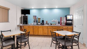 A compact kitchen with wooden cabinets, a countertop with appliances, and a dining area with a table and chairs. - Super 8 by Wyndham Pleasanton (Pleasanton)