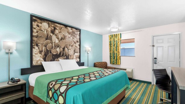 A hotel room with a bed, a desk, a chair, a phone, and a picture on the wall. - Super 8 by Wyndham Pleasanton (Pleasanton)