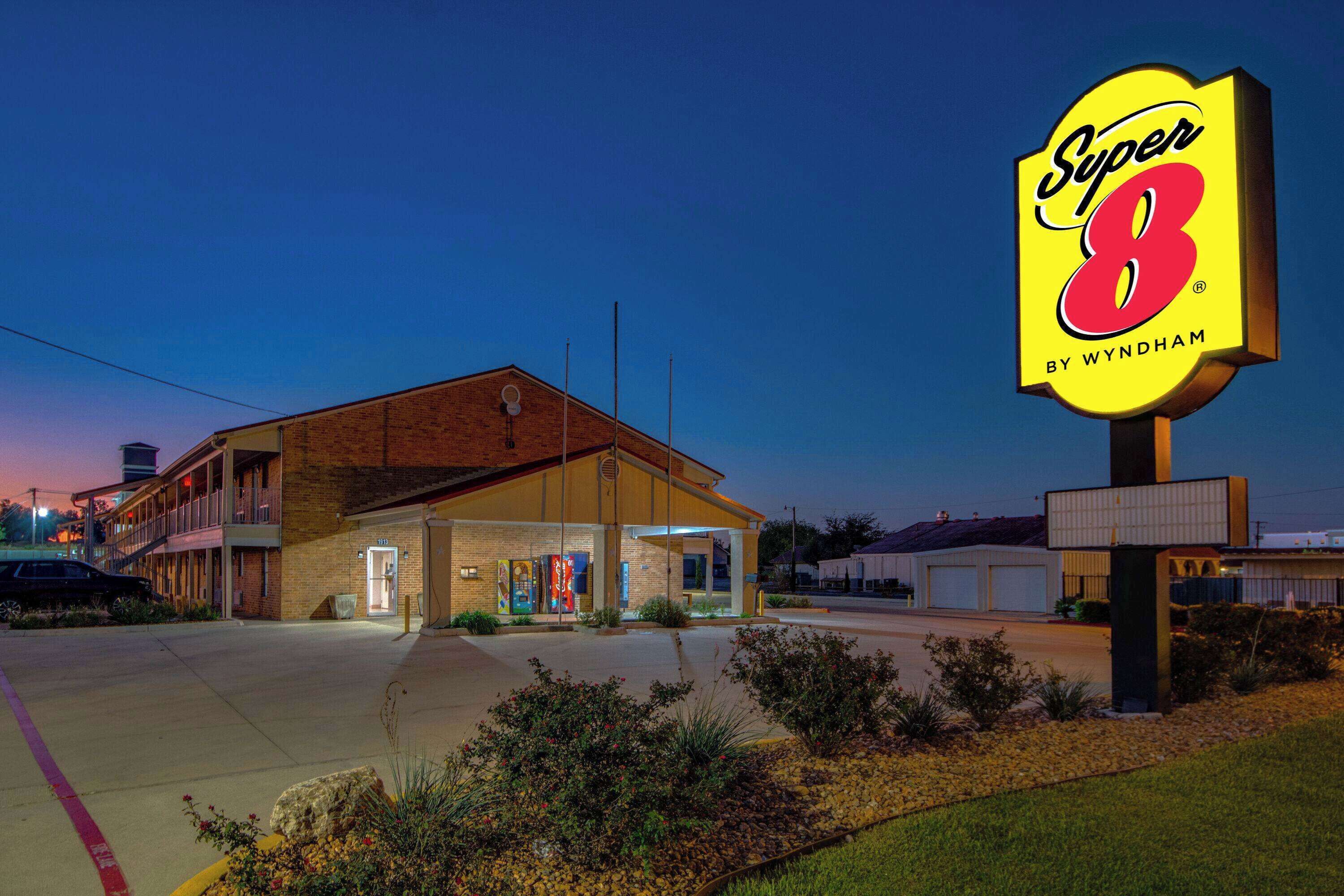 Un motel con un llamativo letrero de 'Super 8', un edificio de ladrillo y un estacionamiento.